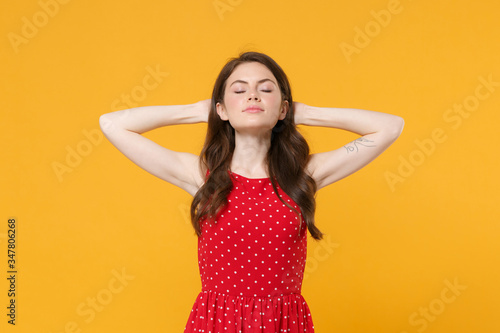 Young brunette woman girl in red summer dress posing isolated on yellow background studio portrait. People sincere emotions lifestyle concept. Mock up copy space. Sleeping with hands behind head.