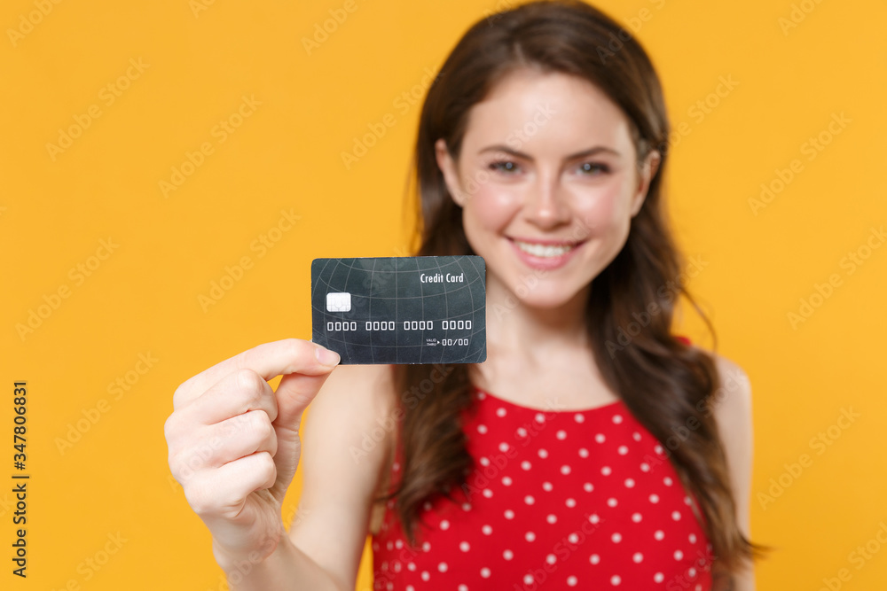 Smiling young brunette woman girl in red summer dress posing isolated on yellow wall background studio portrait. People sincere emotions lifestyle concept. Mock up copy space. Hold credit bank card. Smiling young brunette woman girl in red summer dress posing isolated on yellow wall background studio portrait. People sincere emotions lifestyle concept. Mock up copy space. Hold credit bank card.