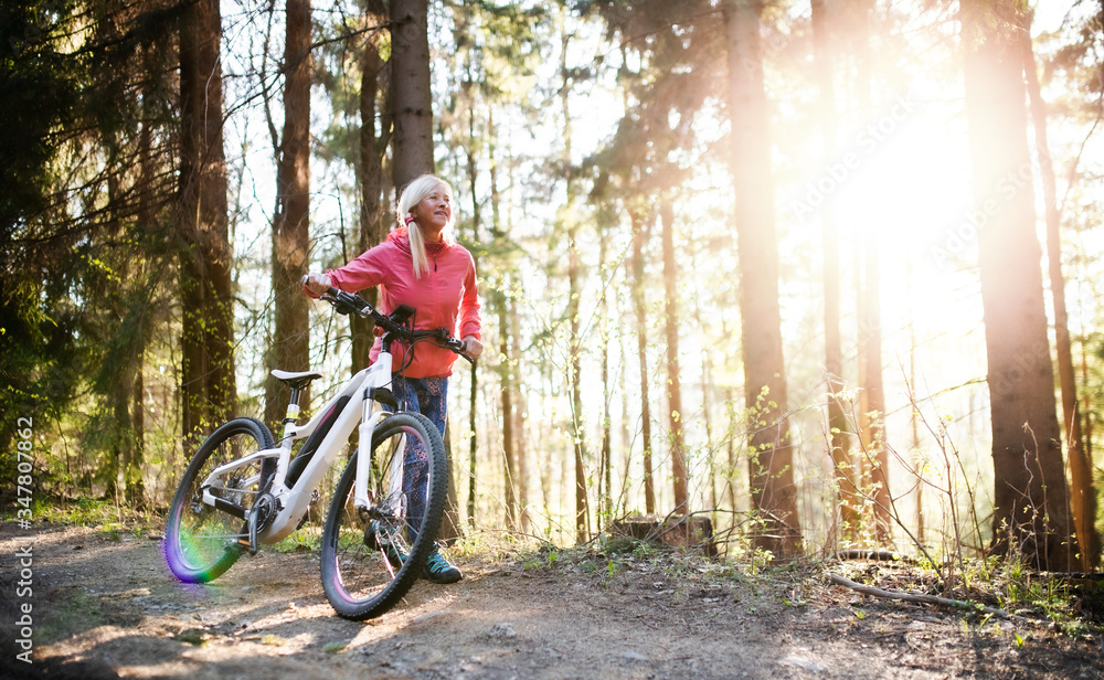 Active senior woman with e-bike cycling outdoors in nature.