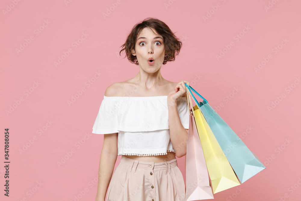 Shocked young woman girl in summer clothes hold package bag with purchases isolated on pastel pink background studio portrait. Shopping discount sale concept. Mock up copy space. Keeping mouth open.