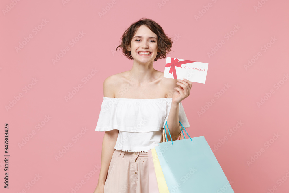 Fototapeta premium Smiling young woman girl in summer clothes isolated on pastel pink background studio portrait. Shopping discount sale concept. Mock up copy space. Hold package bag with purchases, gift certificate.