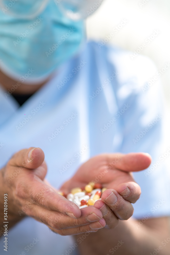 Doctor wearing surgical mask and medical safety goggles holding a handful of medication pills in his hand Doctor wearing surgical mask and medical safety goggles holding a handful of medication pills in his hand