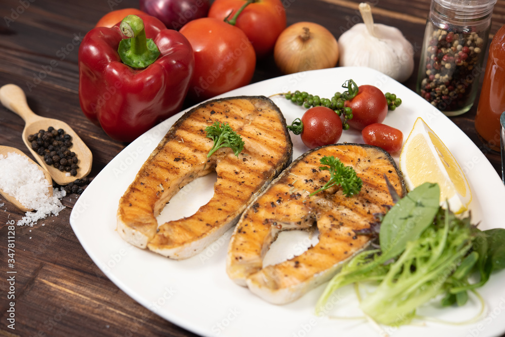 Delicious fillet cut salmon steak in white plate side dish with french fries and salad on dark wood background