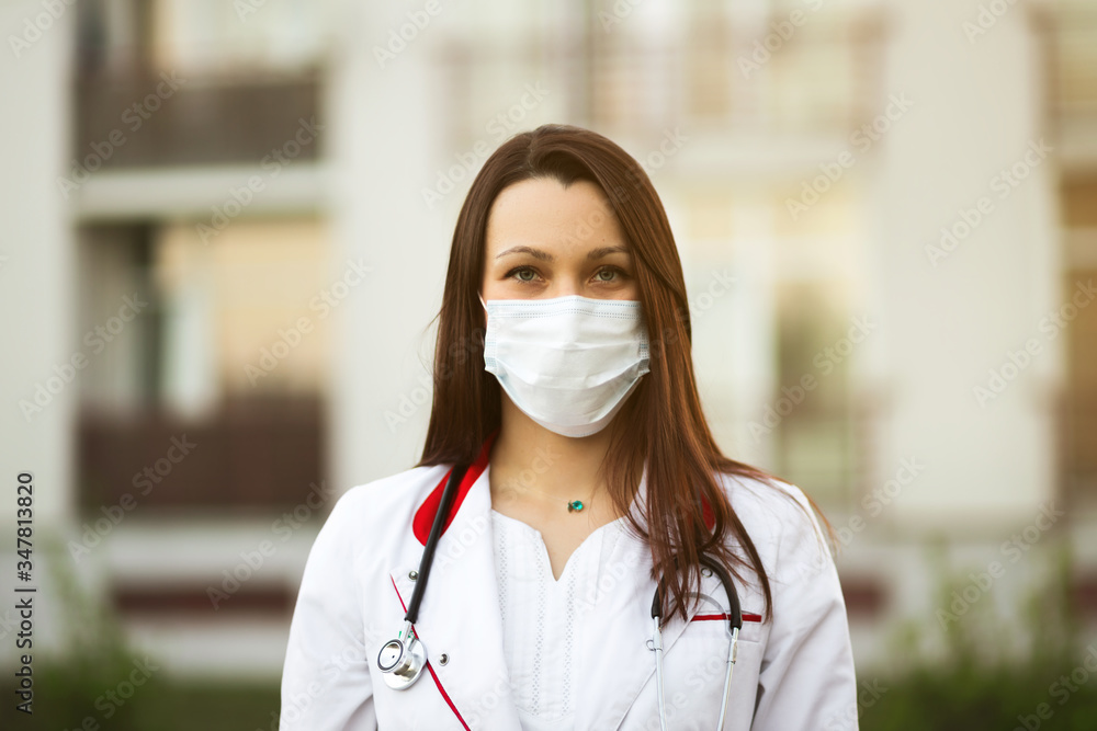 Online webinar or conference concept: Young female doctor in surgical mask and earbuds outdoors Online webinar or conference concept: Young female doctor in surgical mask and earbuds outdoors