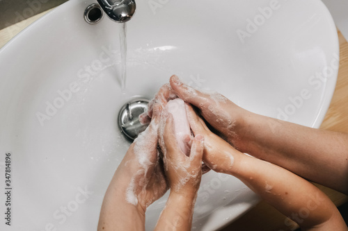 mother carefully washes her child's hands under water in the bathroom in order to prevent coronavirus infection, hands close-up, 4 hands top view