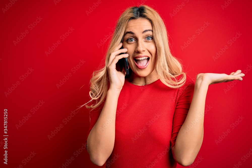 Beautiful blonde woman having conversation talking on the smartphone over red background very happy and excited, winner expression celebrating victory screaming with big smile and raised hands Beautiful blonde woman having conversation talking on the smartphone over red background very happy and excited, winner expression celebrating victory screaming with big smile and raised hands