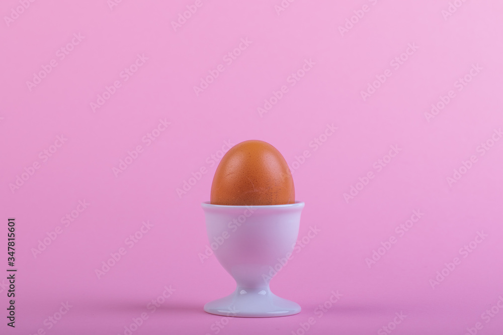 one brown egg in white egg cup before pink background one brown egg in white egg cup before pink background