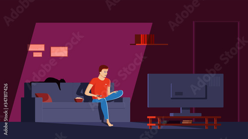 Single man sits in his apartment on the couch, cross-legged, with a remote control in his hand and watches news and movies on TV with a surprised face. A guy in a dark room lit by a TV screen.