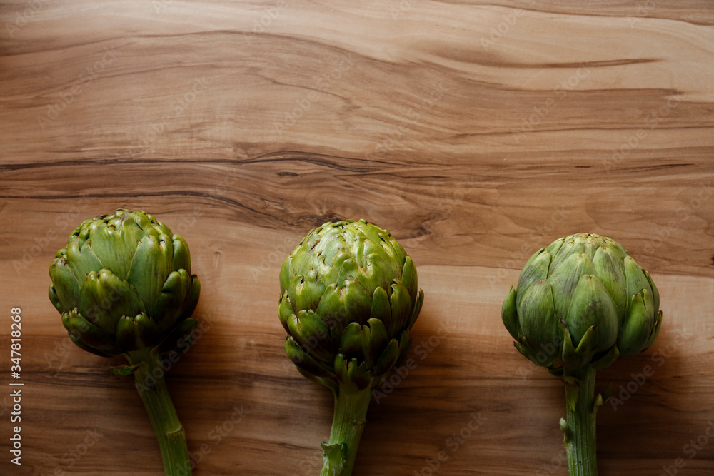 Fototapeta premium Fresh green Italian Artichoke natural wood background. Organic local produce vegetable on textured table. Vegan diet. Clean eating concept. Close up, top view, flat lay.