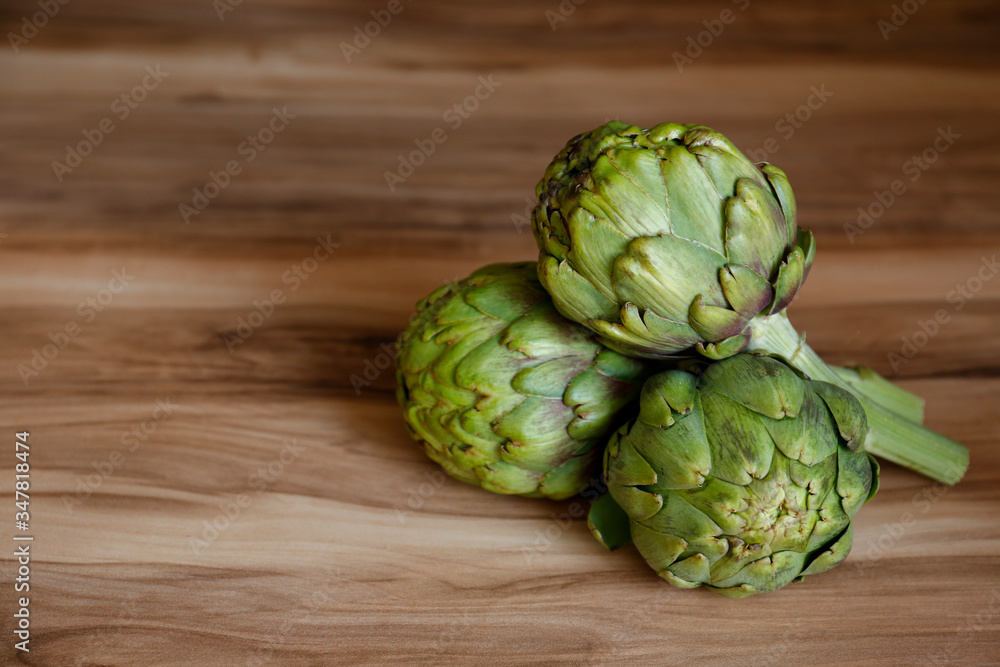 Obraz premium Fresh green Italian Artichoke natural wood background. Organic local produce vegetable on textured table. Vegan diet. Clean eating concept. Close up, top view, flat lay.