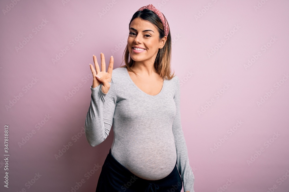 Obraz premium Young beautiful brunette woman pregnant expecting baby over isolated pink background showing and pointing up with fingers number four while smiling confident and happy.