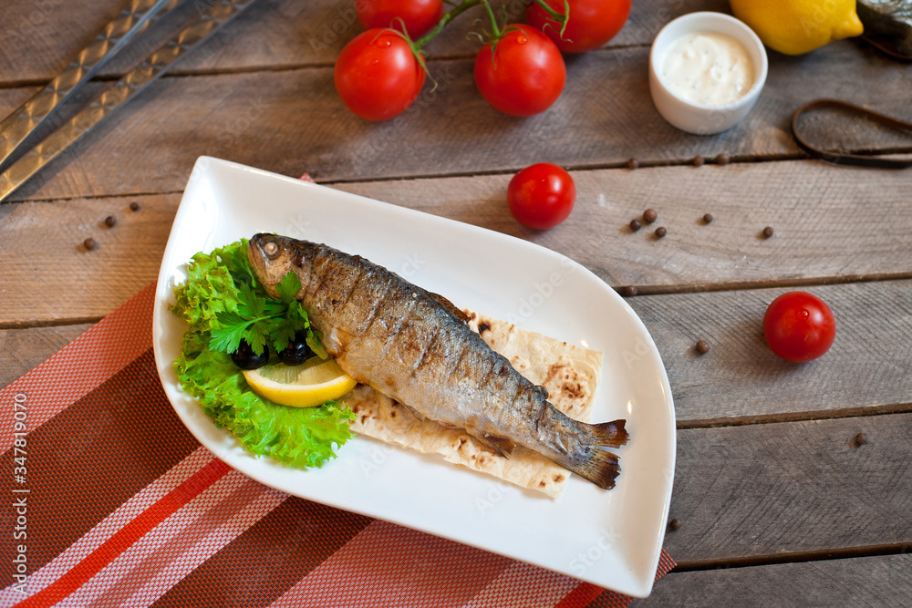 Grilled trout fish with spices, herbs and lemon fried on a grill on a white plate, top view Grilled trout fish with spices, herbs and lemon fried on a grill on a white plate, top view