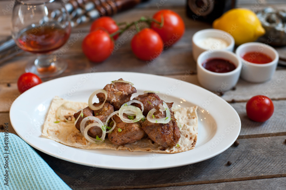 Meat kebab with onions on a white plate on a wooden background. Grilled meat