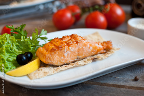 Grilled salmon steak served on a white plate with lemon and herbs. wooden background
