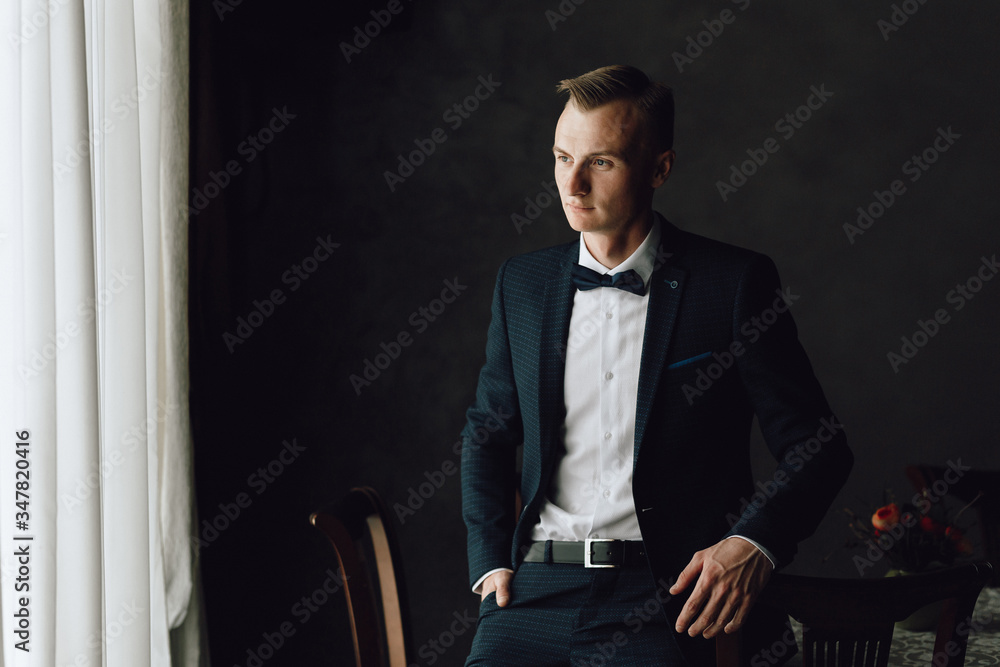 Young blond man in a classic dark suit, businessman. Hands, details, butterfly, blazer, dark background. Young blond man in a classic dark suit, businessman. Hands, details, butterfly, blazer, dark background.