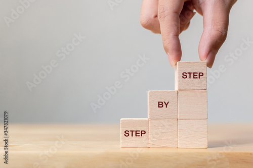 Hand arranging wood block stacking as step stair on top with word Step By Step. Business concept for personal ladder of success process photo