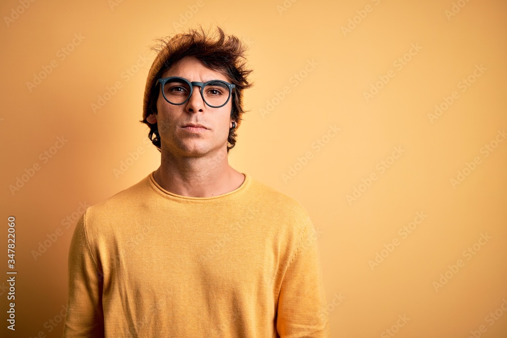 Fototapeta premium Young handsome man wearing casual t-shirt and glasses over isolated yellow background Relaxed with serious expression on face. Simple and natural looking at the camera.