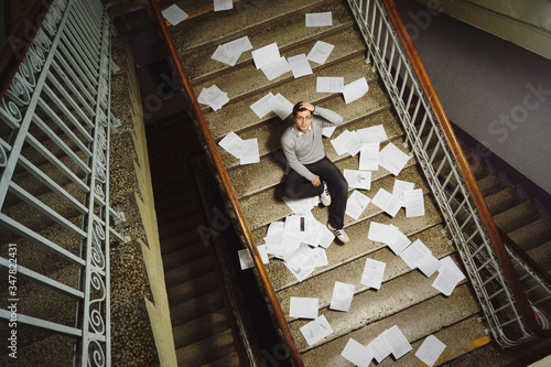 A man sits on a ladder with papers and documents