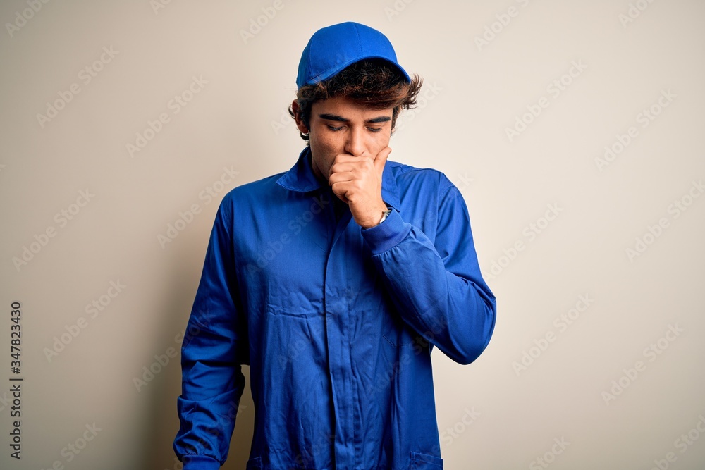 Young mechanic man wearing blue cap and uniform standing over isolated white background feeling unwell and coughing as symptom for cold or bronchitis. Health care concept.