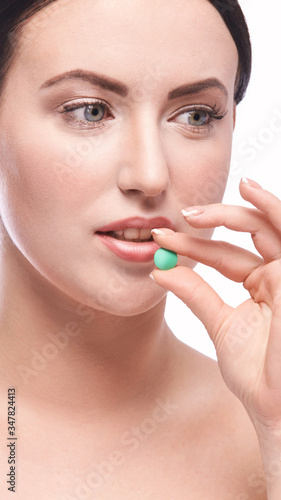 Girl holding a pill. Vitamins concept. Beautiful portrait on white background. Medicine home routine. Female morning supplement. Meds anti allergy drug. Vertical