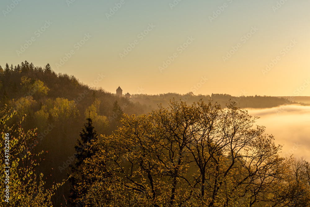 Fototapeta premium A beautiful scene to river Gauja valley and ancient castle Turaida in sunrise at 5 a.m with beutiful fog covering river and surrounding forest, shot was taken in May in Sigulda in Latvia