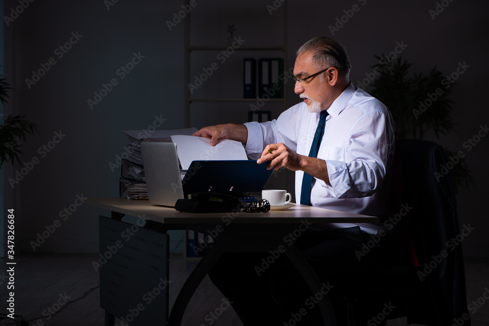 Fototapeta premium Old male employee working late at workplace