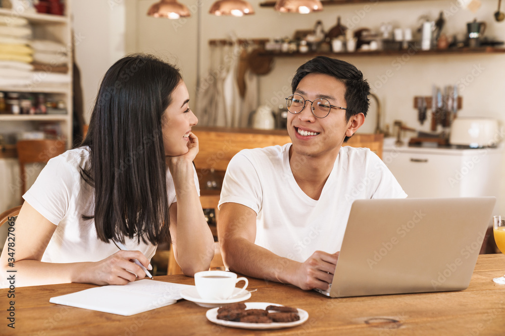 Image of multicultural couple making notes in planner and using laptop Image of multicultural couple making notes in planner and using laptop