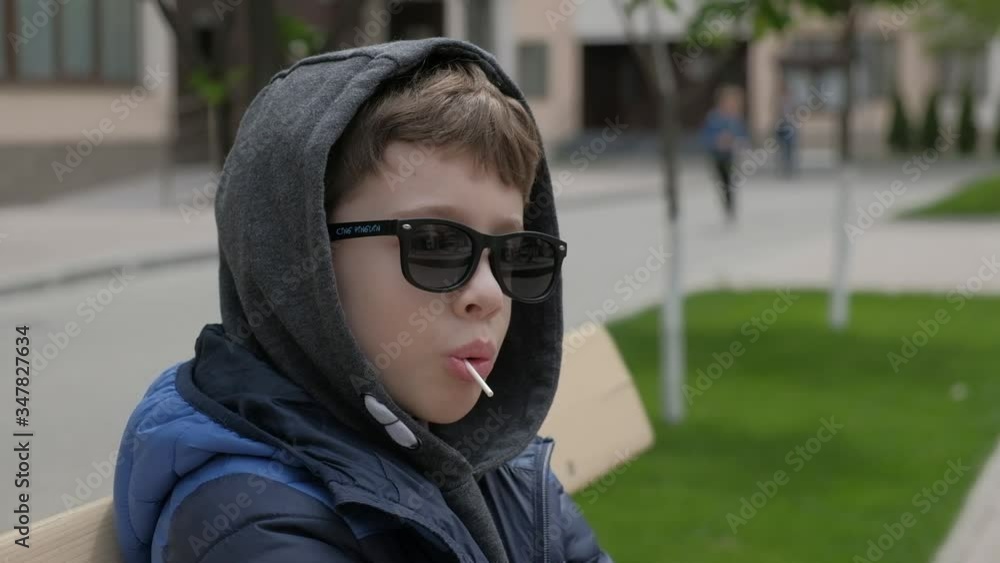 Boy sitting on a bench and eats Lollipop. Rejoices licks the candy, fools around Boy sitting on a bench and eats Lollipop. Rejoices licks the candy, fools around