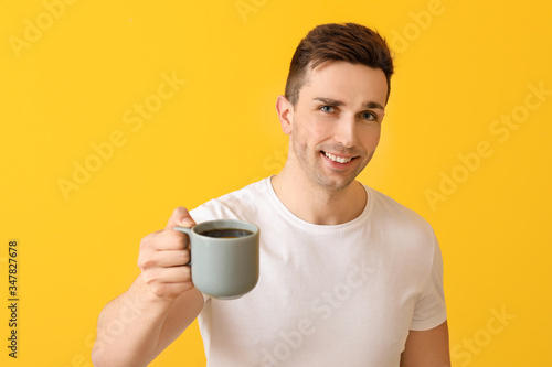 Handsome man with coffee on color background