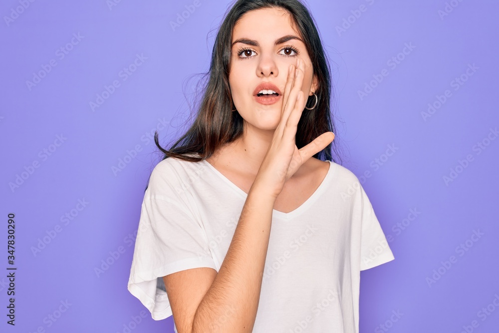 Young beautiful brunette woman wearing casual white t-shirt over purple background hand on mouth telling secret rumor, whispering malicious talk conversation Young beautiful brunette woman wearing casual white t-shirt over purple background hand on mouth telling secret rumor, whispering malicious talk conversation