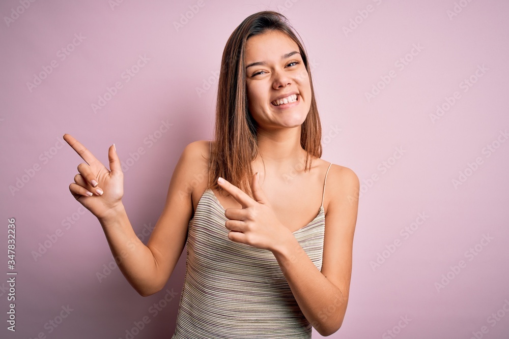 Young beautiful brunette girl wearing casual striped t-shirt over isolated pink background smiling and looking at the camera pointing with two hands and fingers to the side. Young beautiful brunette girl wearing casual striped t-shirt over isolated pink background smiling and looking at the camera pointing with two hands and fingers to the side.