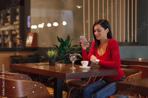 Beautiful young woman suing smartphone and drinking coffee in a cafe