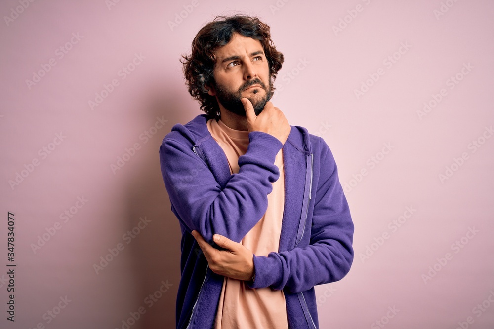 Young handsome sporty man with beard wearing casual sweatshirt over pink background Thinking worried about a question, concerned and nervous with hand on chin Young handsome sporty man with beard wearing casual sweatshirt over pink background Thinking worried about a question, concerned and nervous with hand on chin