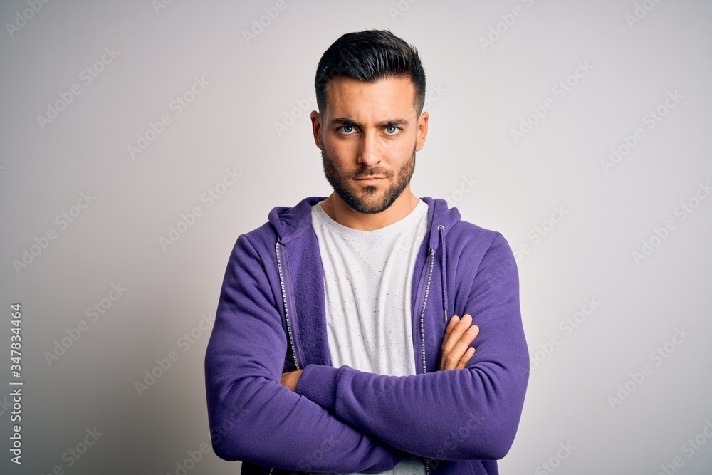 Young handsome man wearing purple sweatshirt standing over isolated white background skeptic and nervous, disapproving expression on face with crossed arms. Negative person. Young handsome man wearing purple sweatshirt standing over isolated white background skeptic and nervous, disapproving expression on face with crossed arms. Negative person.