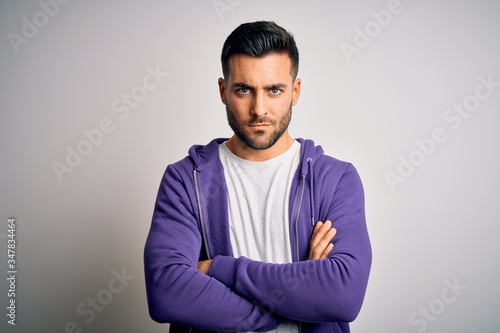 Young handsome man wearing purple sweatshirt standing over isolated white background skeptic and nervous, disapproving expression on face with crossed arms. Negative person.