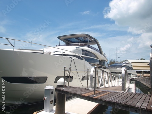The bow of the yacht, the upper deck, portholes of the cabins, board, and gangway with wooden flooring and handrails. Luxury white yacht moored at the marina of the yacht club. Pier and motoryacht