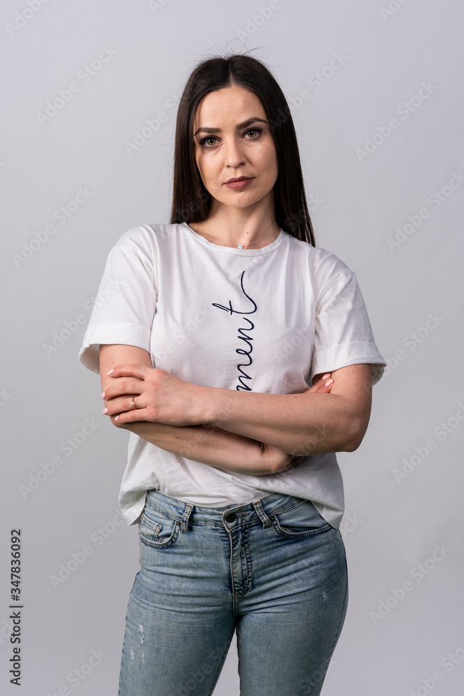Slender girl in a white t-shirt and jeans folded his hands in front of him and looks directly into the camera Slender girl in a white t-shirt and jeans folded his hands in front of him and looks directly into the camera