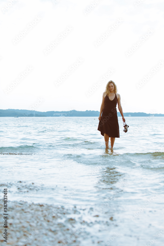 Obraz premium woman in black light dress walking barefoot by sea beach