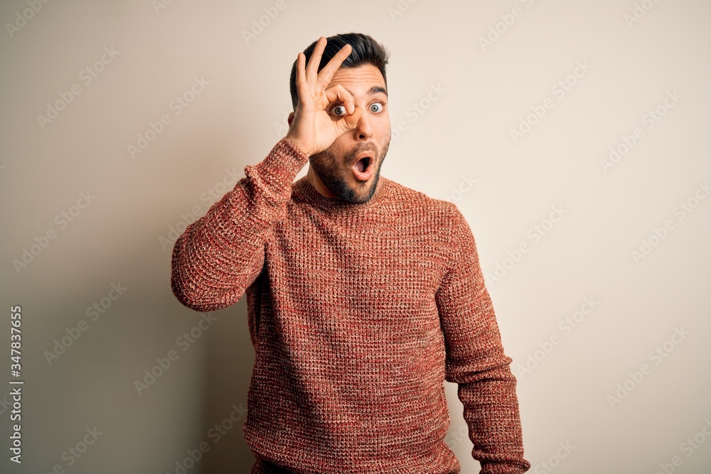 Young handsome man wearing casual sweater standing over isolated white background doing ok gesture shocked with surprised face, eye looking through fingers. Unbelieving expression. Young handsome man wearing casual sweater standing over isolated white background doing ok gesture shocked with surprised face, eye looking through fingers. Unbelieving expression.