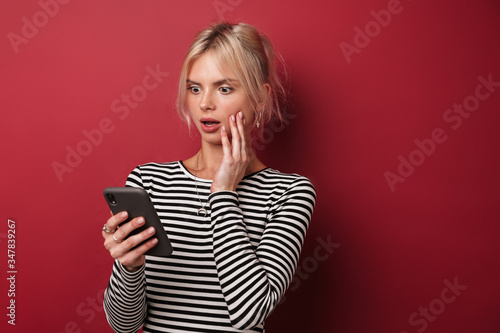 Image of nice shocked woman in striped sweatshirt typing on cellphone