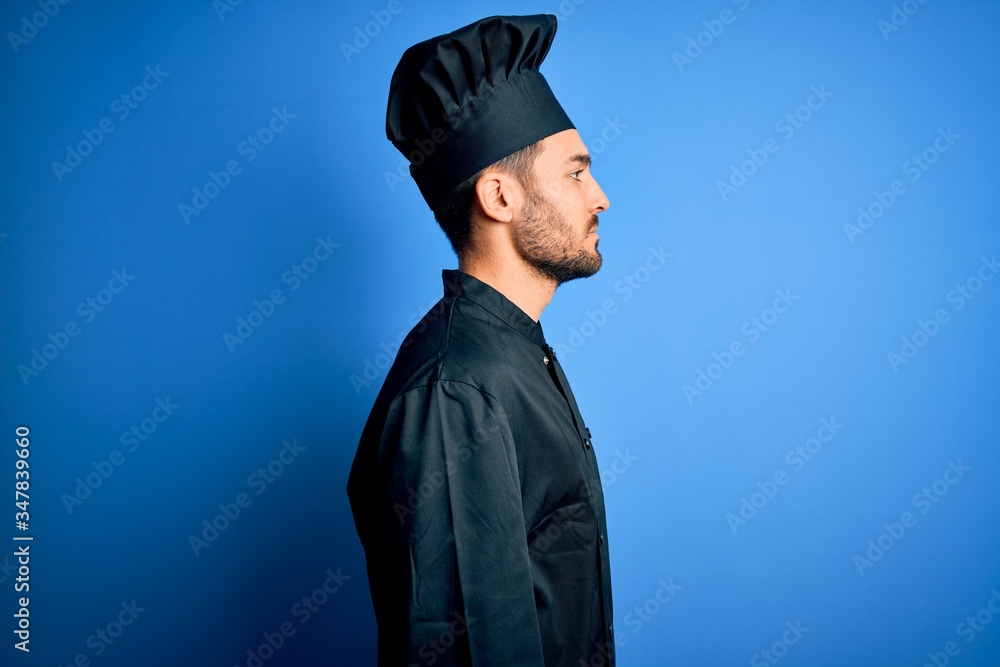 Young handsome chef man with beard wearing cooker uniform and hat over blue background looking to side, relax profile pose with natural face with confident smile. Young handsome chef man with beard wearing cooker uniform and hat over blue background looking to side, relax profile pose with natural face with confident smile.