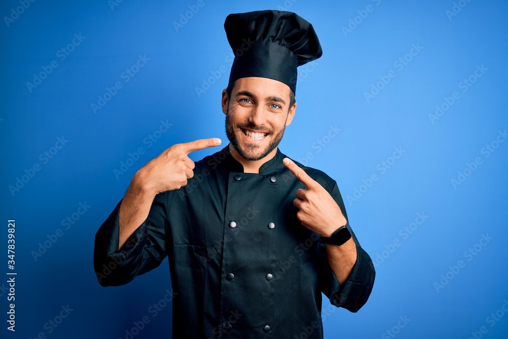 Young handsome chef man with beard wearing cooker uniform and hat over blue background smiling cheerful showing and pointing with fingers teeth and mouth. Dental health concept. Young handsome chef man with beard wearing cooker uniform and hat over blue background smiling cheerful showing and pointing with fingers teeth and mouth. Dental health concept.