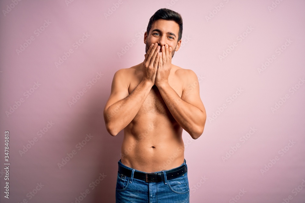 Fototapeta premium Young handsome strong man with beard shirtless standing over isolated pink background laughing and embarrassed giggle covering mouth with hands, gossip and scandal concept