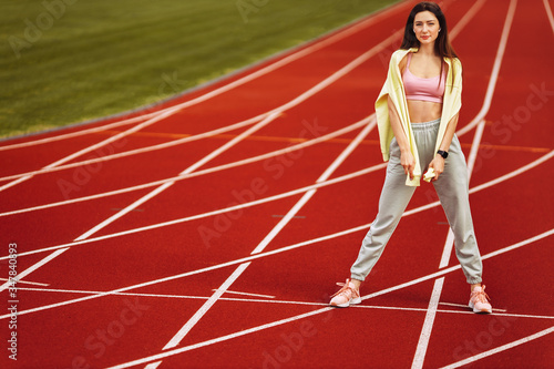 Beautiful young woman in sports wear looking at camera standing on the red stadium