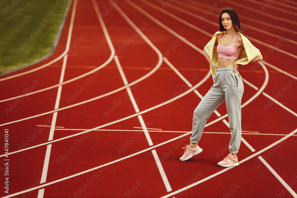 Obraz premium Beautiful young woman in sports wear looking at camera standing on the red stadium
