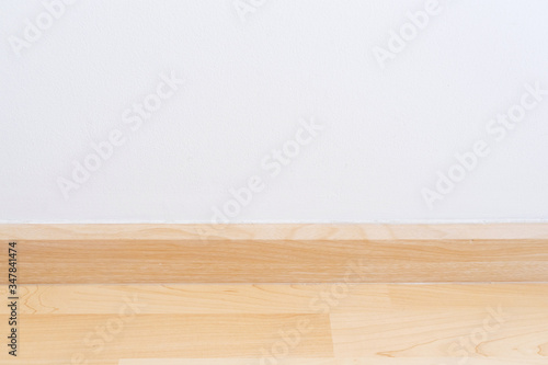 Wooden wall base skirting, finishing material with wood laminate floor and white mortar wall. Empty room with white wall and wooden floor.