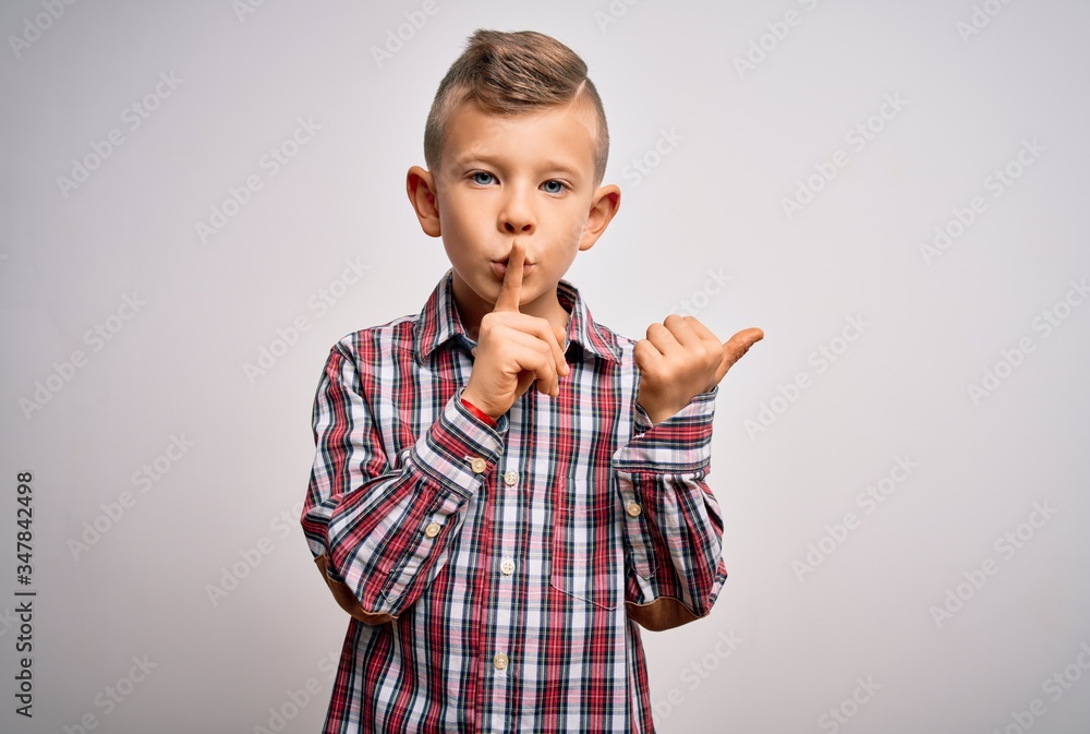Young little caucasian kid with blue eyes wearing elegant shirt standing over isolated background asking to be quiet with finger on lips pointing with hand to the side. Silence and secret concept. Young little caucasian kid with blue eyes wearing elegant shirt standing over isolated background asking to be quiet with finger on lips pointing with hand to the side. Silence and secret concept.