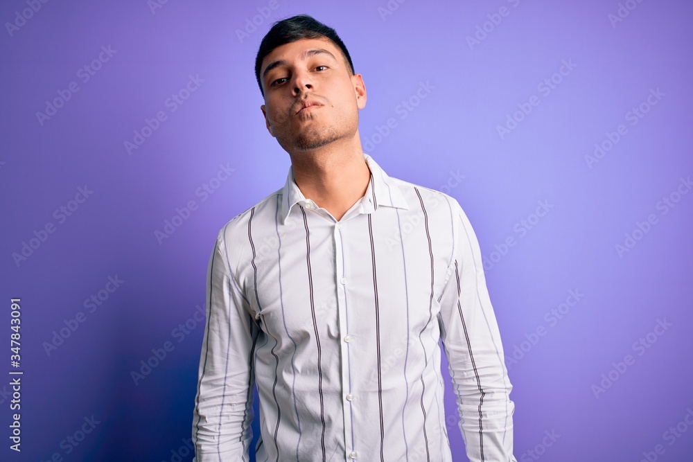 Young handsome hispanic man wearing elegant business shirt standing over purple background looking at the camera blowing a kiss on air being lovely and sexy. Love expression. Young handsome hispanic man wearing elegant business shirt standing over purple background looking at the camera blowing a kiss on air being lovely and sexy. Love expression.