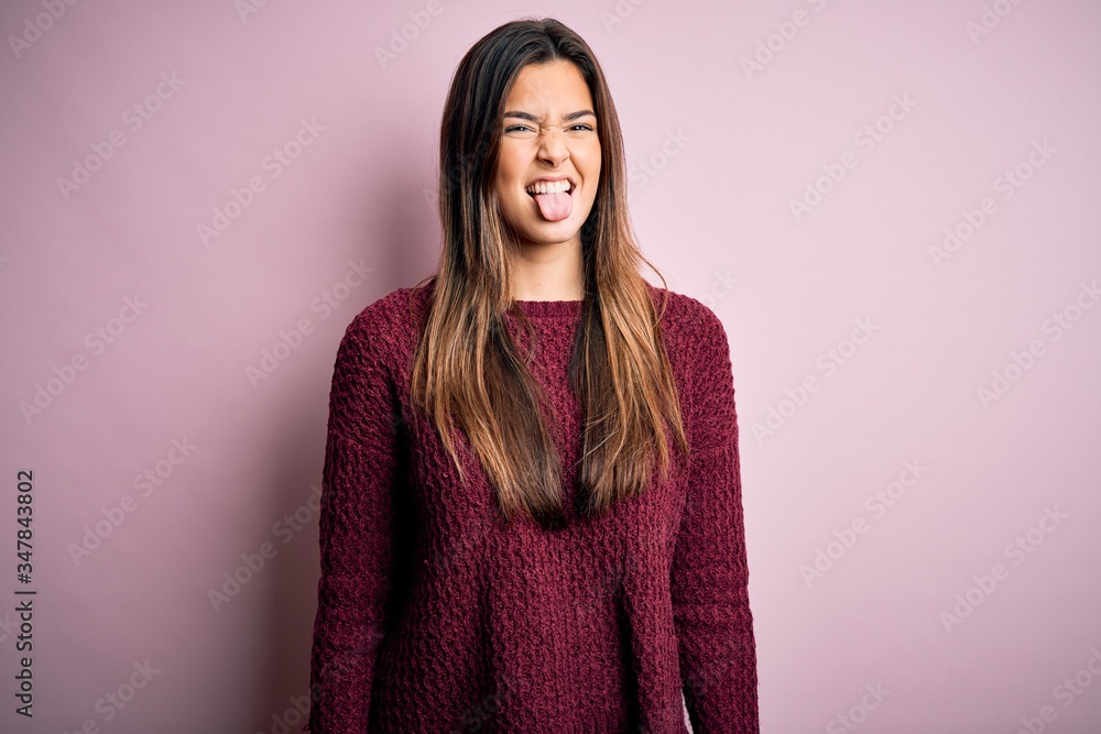 Young beautiful girl wearing casual sweater over isolated pink background sticking tongue out happy with funny expression. Emotion concept. Young beautiful girl wearing casual sweater over isolated pink background sticking tongue out happy with funny expression. Emotion concept.