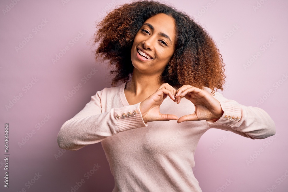 Young african american woman with afro hair wearing casual sweater over pink background smiling in love doing heart symbol shape with hands. Romantic concept. Young african american woman with afro hair wearing casual sweater over pink background smiling in love doing heart symbol shape with hands. Romantic concept.
